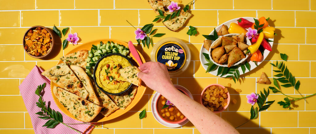 grouping of dip-able foods with hand dipping into a container of Oolie yellow curry