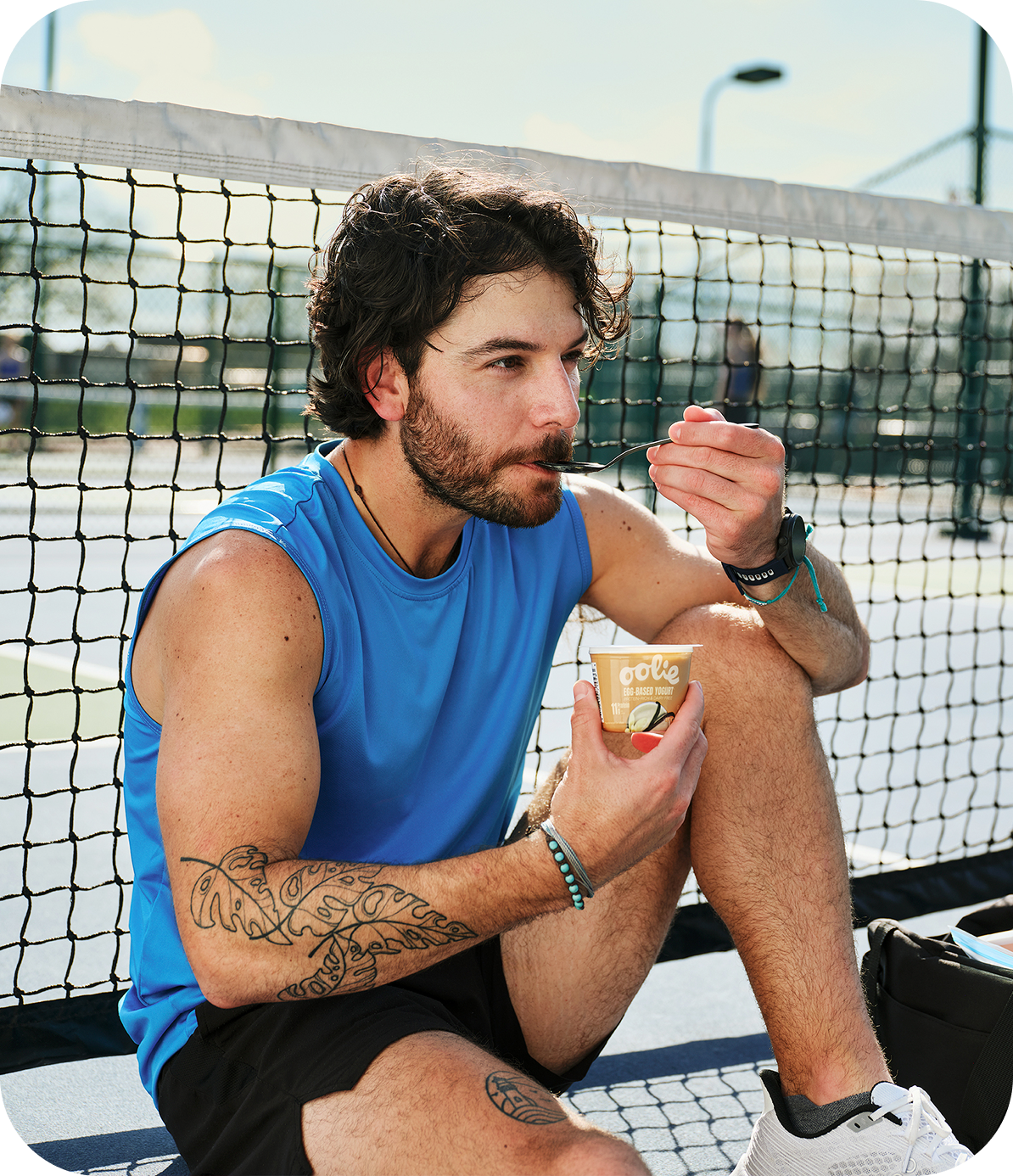 Athlete eating a cup of Oolie yogurt on a tennis court