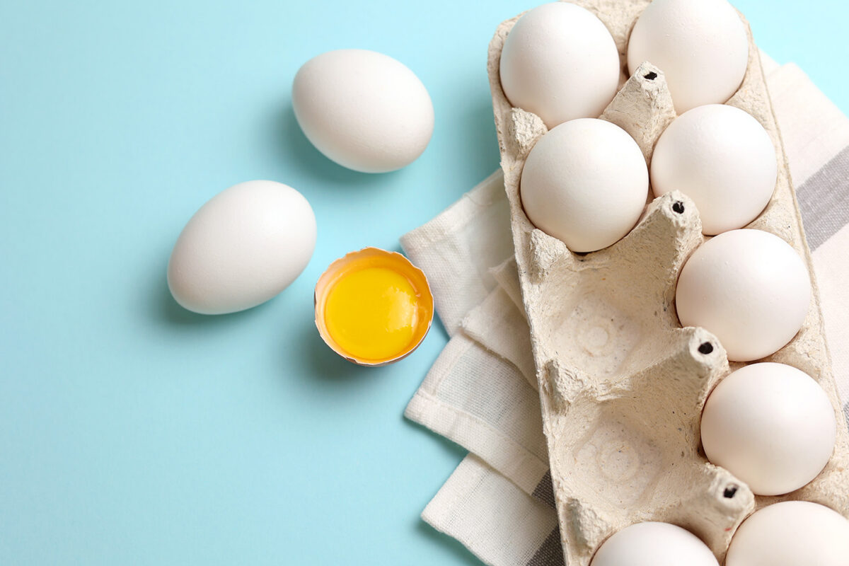 carton of eggs with one cracked open showing yolk
